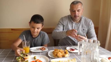 Baba ve oğul masada oturmuş, yemek yiyor ve içki içiyorlar..
