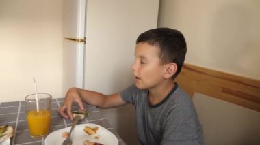 Çocuk masada oturuyor, yemek yiyor ve meyve suyu içiyor..