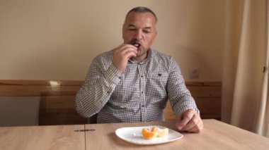 Bir adam masada otururken portakal yiyor..