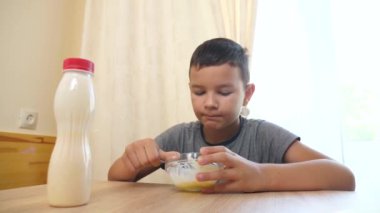Bir çocuk masada otururken kaşıkla yoğurt yiyor..