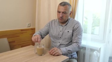 Adam kahveye şeker ekliyor ve kaşıkla karıştırıyor..