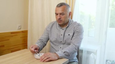 Bir adam masada otururken kaşıkla dondurma yiyor..