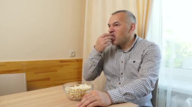 Bir adam masada oturuyor ve patlamış mısır yiyor..