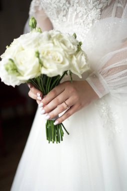 Düğün töreni. Parmağında yüzük olan beyaz elbiseli gelin elinde bir buket gül tutuyor..