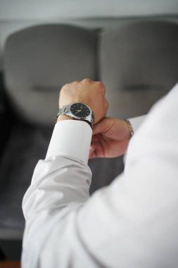Şık bir erkek aksesuarı. Bir adam bileğinde metal bir bileklikle saati takar..