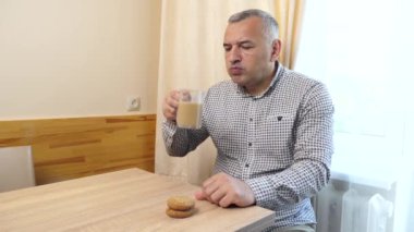 Bir adam masada oturuyor, kurabiye yiyor ve kahve içiyor..