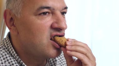 Bir adam masada oturuyor, kurabiye yiyor ve kahve içiyor..