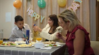 Bir çocuğun doğum gününü kutlarken, insanlar masaya oturur, içki içer ve kendilerini ödüllendirirler. Doğum günü kutlaması.