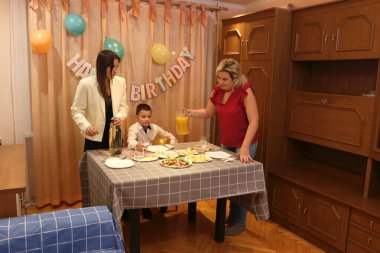 Bir anne, kızı ve oğluyla birlikte doğum günü kutlaması için şenlik masasına servis yapıyor. Yumuşak ışıklandırma.