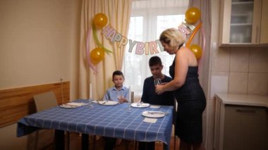 Bir anne, oğlu ve yeğeniyle birlikte doğum gününde şenlik masasına servis yapar. Doğum günü kutlaması.