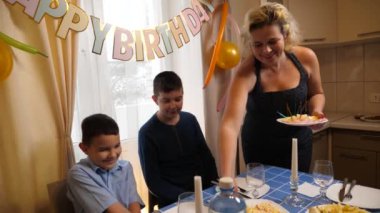 Bir anne, oğlu ve yeğeniyle birlikte doğum gününde şenlik masasına servis yapar. Doğum günü kutlaması.