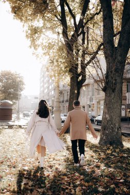 Bir adam ve aşık bir kız parkta sonbahar yaprakları üzerinde yürüyorlar..