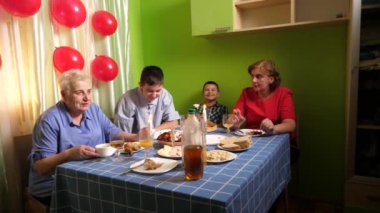 Büyükannenin doğum gününü kutlayan konuklar masaya oturur, içer ve kendilerini ödüllendirirler. Doğum günü kutlaması.