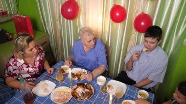 Büyükannenin doğum gününü kutlayan konuklar masaya oturur, içer ve kendilerini ödüllendirirler. Doğum günü kutlaması.