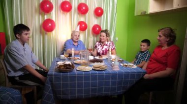 Büyükannenin doğum gününü kutlayan konuklar masaya oturur, içer ve kendilerini ödüllendirirler. Doğum günü kutlaması.