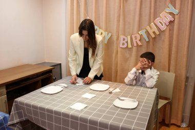 Bir anne, kızı ve oğluyla birlikte doğum günü kutlaması için şenlik masasına servis yapıyor. Yumuşak ışıklandırma.