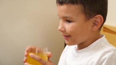 Bir çocuk masada otururken bardaktan soda içer..