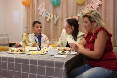 Çocuğun doğum gününü kutlayan konuklar masaya oturur, içer ve kendilerini ödüllendirirler. Doğum günü kutlaması.