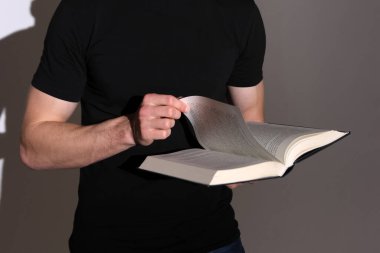 Siyah elbiseli bir adam, elinde tuttuğu bir kitabı çevirir..