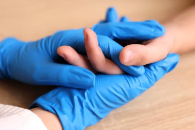 Tıbbi eldivenli bir doktor çocuğun elini tutar. Etkileşim ve destek.