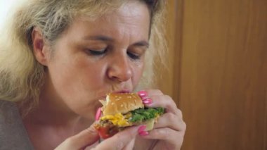 Bir kadın masada otururken hamburger yiyor..