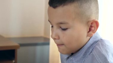 Çocuk masada otururken bir hamburger yiyor..