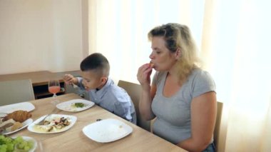 Anne ve oğlu masada otururken hamburger yiyorlar..