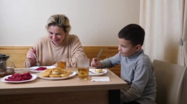 Anne ve oğul mutfakta ev yapımı bulaşıklarla yemek yiyorlar..