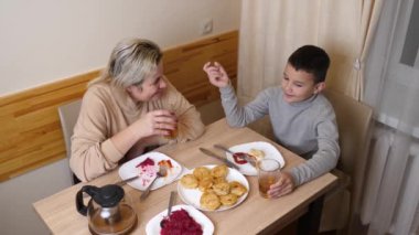 Anne ve oğul mutfakta ev yapımı bulaşıklarla yemek yiyorlar..