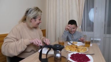 Anne ve oğul mutfakta ev yapımı bulaşıklarla yemek yiyorlar..