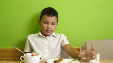 Çocuk masada otururken bir sandviç yiyor..