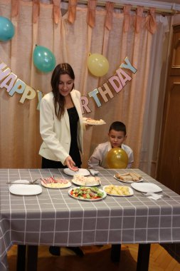 Çocuğun doğum gününü kutlayan konuklar masaya oturur, içer ve kendilerini ödüllendirirler. Doğum günü kutlaması.