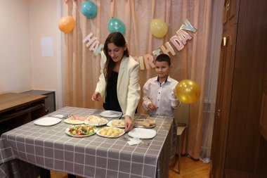 Çocuğun doğum gününü kutlayan konuklar masaya oturur, içer ve kendilerini ödüllendirirler. Doğum günü kutlaması.