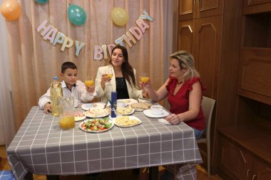 Çocuğun doğum gününü kutlayan konuklar masaya oturur, içer ve kendilerini ödüllendirirler. Doğum günü kutlaması.