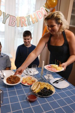 Oğlu ve yeğeniyle birlikte bir kadın doğum günü kutlaması için bir oda ve şenlik masası dekore ediyor. Yumuşak ışıklandırma.