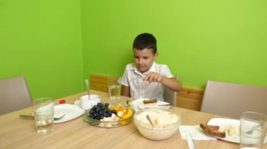 Çocuk masada otururken meyve yer..
