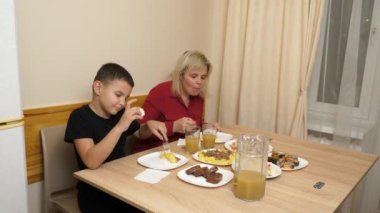 Anne ve oğlu festival masasına oturur ve lezzetli yemeklerin tadını çıkarırlar. Evde kutlarız..