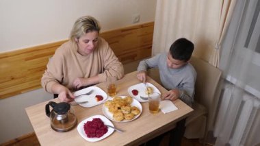 Anne ve oğul mutfakta ev yapımı bulaşıklarla yemek yiyorlar..