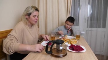 Anne ve oğul mutfakta ev yapımı bulaşıklarla yemek yiyorlar..