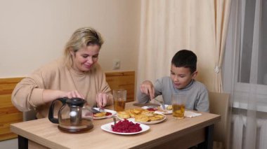 Anne ve oğul mutfakta ev yapımı bulaşıklarla yemek yiyorlar..