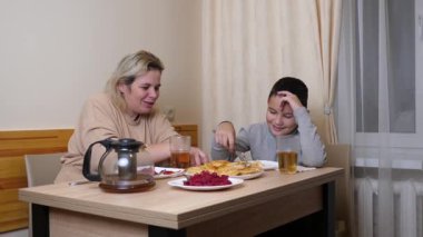 Anne ve oğul mutfakta ev yapımı bulaşıklarla yemek yiyorlar..