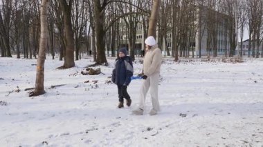 Küçük kardeşiyle bir kız karlı bir parkta yürüyor ve eğleniyor..