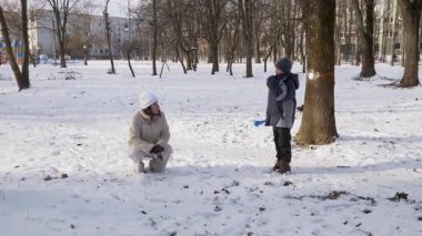 Küçük kardeşiyle bir kız karlı bir parkta yürüyor ve eğleniyor..