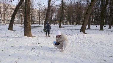 Küçük kardeşiyle bir kız karlı bir parkta yürüyor ve eğleniyor..