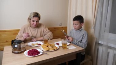 Anne ve oğul mutfakta ev yapımı bulaşıklarla yemek yiyorlar..