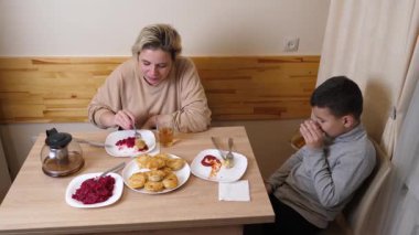 Anne ve oğul mutfakta ev yapımı bulaşıklarla yemek yiyorlar..