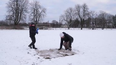 Bir kadın ve oğlu karda halı temizler ve eğlenirler..
