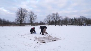Bir kadın ve oğlu karda halı temizler ve eğlenirler..