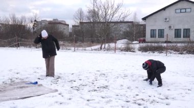 Bir kadın ve oğlu karda halı temizler ve eğlenirler..
