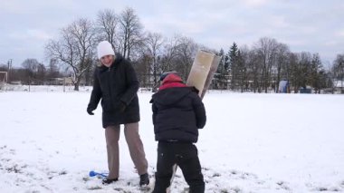 Bir kadın ve oğlu karda halı temizler ve eğlenirler..